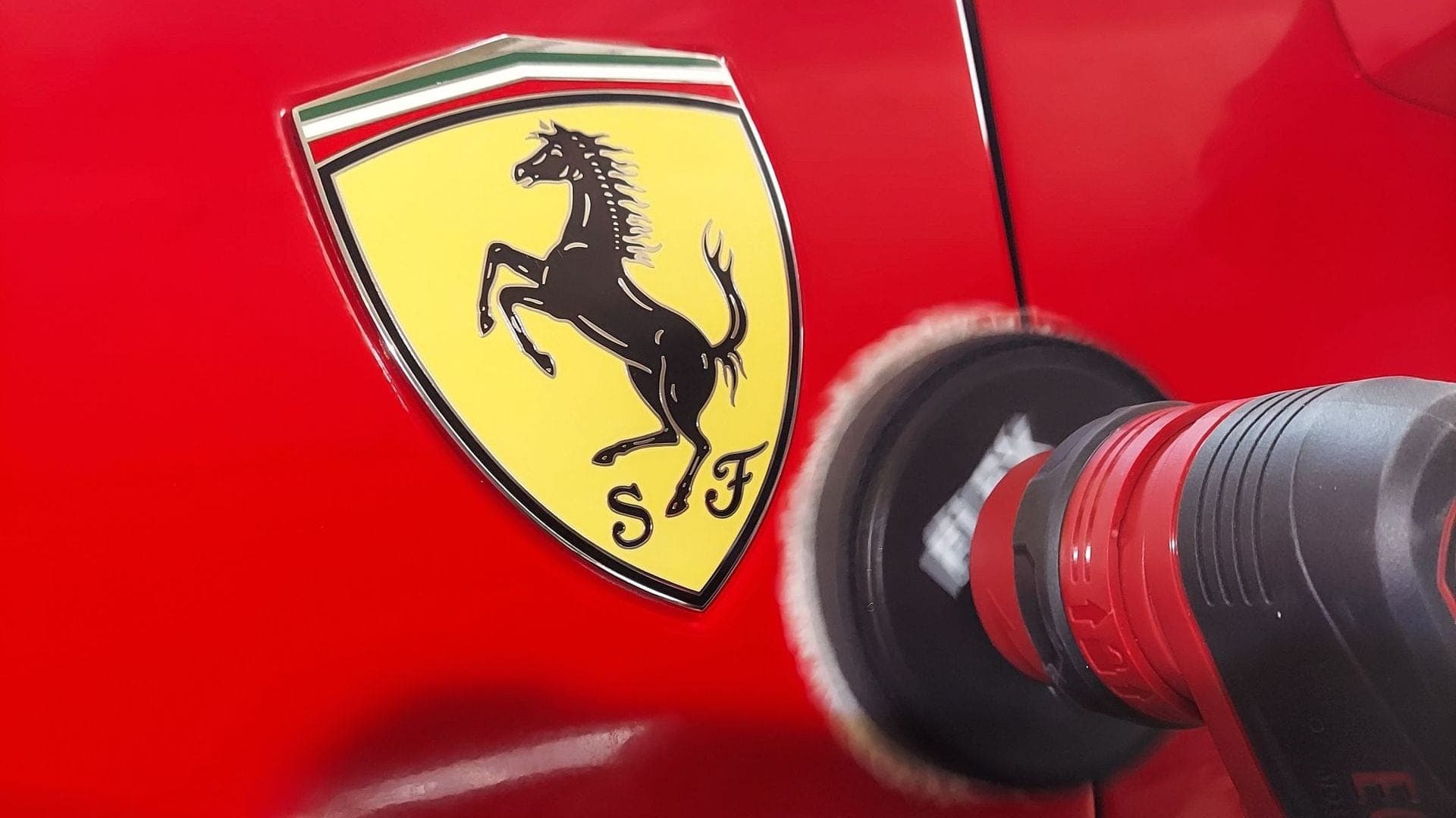 Rotary polisher buffing red paint next to a Ferrari shield badge