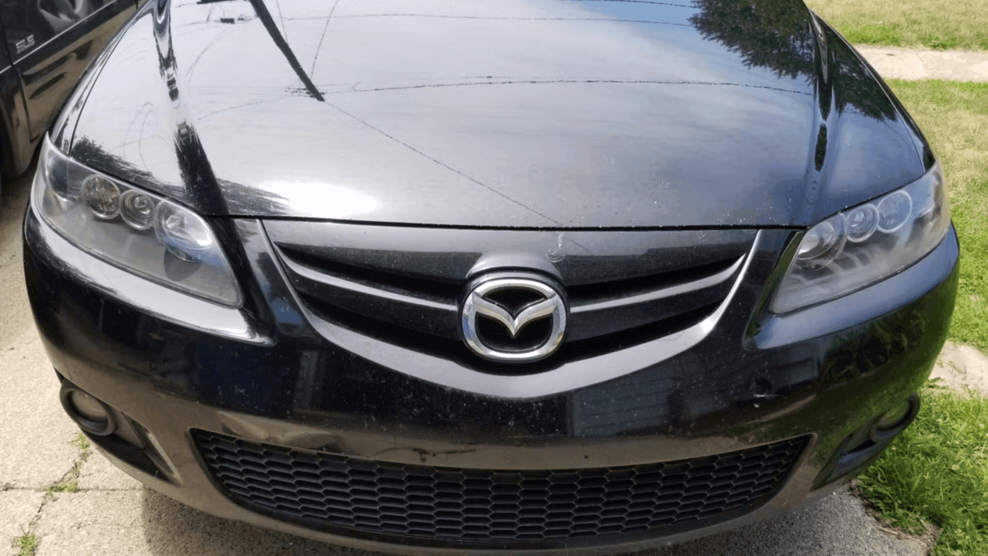 Front of a black Mazda sedan with clear headlights, parked on a driveway