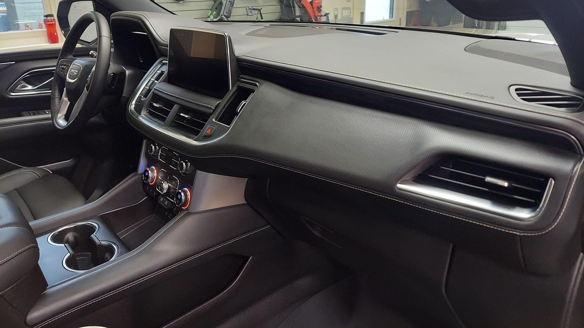 Modern car interior with black leather dashboard, white contrast stitching, and a central infotainment screen.