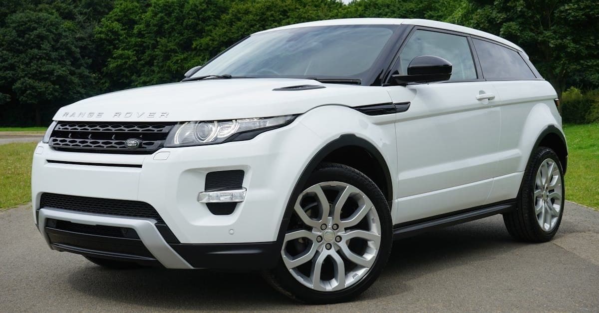 White Range Rover Evoque parked on a paved road with trees behind it